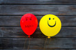 © 9dreamstudio - Treat depression concept. Balloons with frustrated and smiling faces on dark wooden background top view