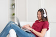 © weedezign - Asian woman listening music on headphone and using laptop computer with relax pose at couch in living room at home.leisure lifestyle