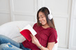 © weedezign - Asian woman listening music on headphone and reading book with relax pose at couch in living room at home.leisure lifestyle