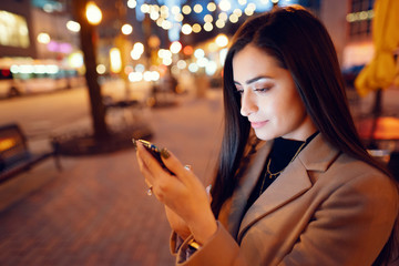 Beautiful girl in a evening city. Stylish brunette in a brown coat. Woman in a Chicago. Lady with a phone