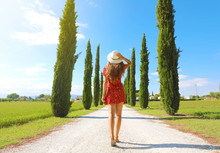 Travel In Tuscany. Young Woman Walking In Beautiful And Idyllic Landscape Of A Lane Of Cypresses In The Italian Countryside Of Tuscany.