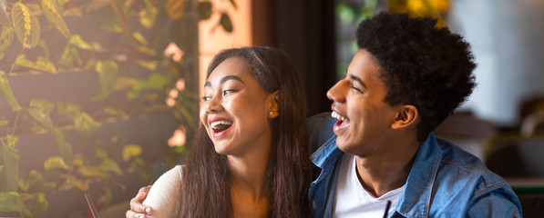 Wall Mural - Afro guy and mixed race girl laughing together in cafe