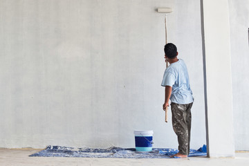 Back view of construction worker standing painting wall of new house building at construction site. Real people.