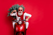 © deagreez - Portrait of cheerful pensioner carrying fir tree having eyeglasses eyewear drive bike wearing white jumper isolated over red background