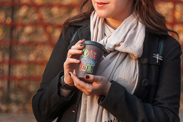  girl holds paper cup with coffee in the background of autumn park