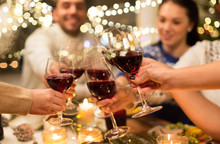Holidays And Celebration Concept - Close Up Of Happy Friends Having Christmas Dinner At Home, Drinking Red Wine And Clinking Glasses