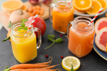 Wall Mural - food , healthy eating and vegetarian concept - mason jar glasses of orange and carrot juices with paper straws, fruits and vegetables on slate table