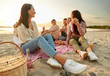 © Syda Productions - friendship, leisure and fast food concept - group of happy friends eating sandwiches or burgers at picnic on beach in summer