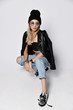 © Dmitry Lobanov - Grunge style woman in torn jeans, bralet, silver boots with untied shoelaces and knitted hat sitting squatting on white