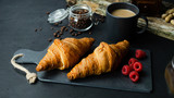 Croissant z malinami leżący na kamiennej desce. Ciemne tło, widok z góry.