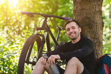 Portrait Of Smiling Cyclist Resting Under Tree In Mountain Forest