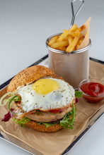 Close Up Of Juicy Beef Burger With Fried Egg And Crispy French Fries On A Tray With Craft Paper Isolated On White Flat Lay