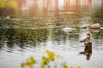 Wall Mural - Fisherman using rod fly fishing in mountain river autumn splashing water