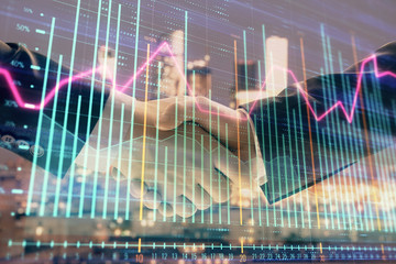 Double exposure of financial graph on cityscape background with two businessman handshake. Concept of stock market deal