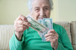© berna_namoglu - A senior woman holding and giving American Dollars