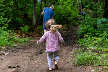 Wall Mural - Diverse people enjoy spiritual gathering A playful young girl with blonde hair and a pink jumper is seen running towards her father on a woodland trail during a camping trip.