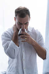 Wall Mural - front view of depressed man in shirt drinking cognac at home