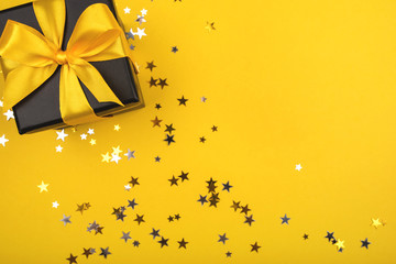 Wall Mural - Gift box on yellow background with sparkling confetti.