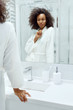 © puhhha - Skin care. Woman applying face cream looking in bathroom mirror