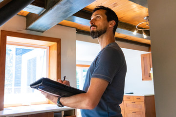 Indoor damp & air quality (IAQ) testing. A close up and side view of a tall caucasian male with short black hair and beard, inspecting a home during an indoor environmental quality assessment.