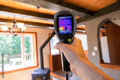 Indoor damp & air quality (IAQ) testing. A first person perspective holding an infrared thermal vision device, showing heat sources and cold spots inside a family room with copy space.