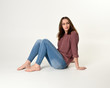 © faestock - full length portrait of brunette woman wearing jeans and pink jumper. seated pose with a white studio background.
