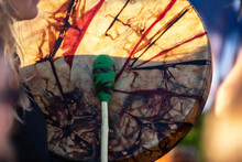 Sacred Drums During Spiritual Singing. A Close Up View Of A Traditionally Dyed Colorful Native Drum And Beater In The Hands Of A Musician During A Daytime Music Celebration.