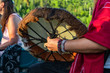 © Valmedia - Sacred drums during spiritual singing. A close up view on the arm and hand of a person wearing a red shirt and colorful beads, holding a traditionally crafted native drum with furry edge strip.