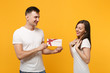 © ViDi Studio - Pretty young couple two friends guy girl in white empty blank design t-shirts posing isolated on yellow orange wall background. People lifestyle concept. Mock up copy space. Holding gift certificate.
