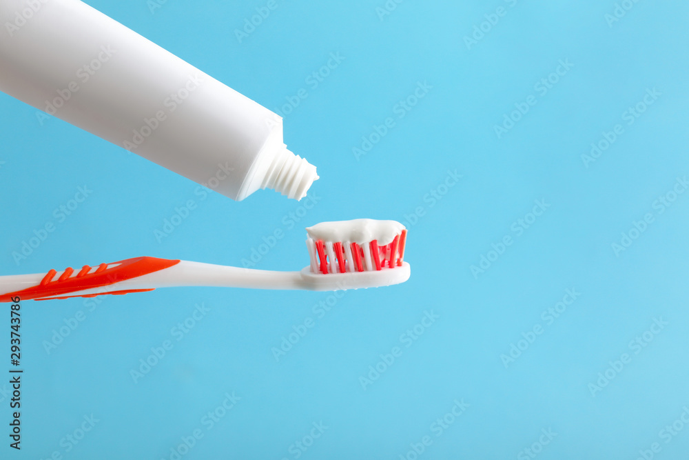 Squeezing of tooth paste from tube onto brush against color background