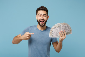 Wall Mural - Young excited man in casual clothes posing isolated on blue background, studio portrait. People lifestyle concept. Mock up copy space. Pointing index finger on fan of cash money in dollar banknotes.