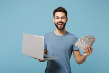 Young Smiling Joyful Man In Casual Clothes Posing Isolated On Blue Wall Background. People Lifestyle Concept. Mock Up Copy Space. Holding Laptop Pc Computer, Fan Of Cash Money In Dollar Banknotes.