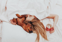 Beautiful Girl Lying Relax In Bed With Her Beloved Dog. Morning Prodding In A Warm Comfortable Bed. Cute Woman And Her Dog Are Sleeping In The Bed Covered With A Blanket. - Image  
