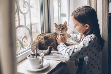 Wall Mural - Child relaxing with a cat on a window sill