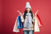 Excited Woman In Winter Sweater, Scarf And Hat Holding Shopping Bags, Isolated On Red