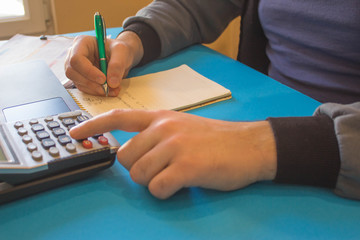 man writing notes from computer on table. Man hand with pen, calculator and computer