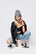 © Dmitry Lobanov - Punk style girl in torn jeans, leather top, leather jacket, chrome boots and knitted hat brutal sitting squatting