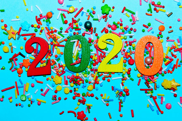 Colorful Christmas background. Holidays, Christmas, New Year concept. Multi-colored numbers 2020 and scattered candies on a blue background.