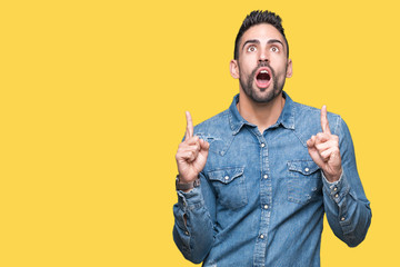 Young handsome man over isolated background amazed and surprised looking up and pointing with fingers and raised arms.