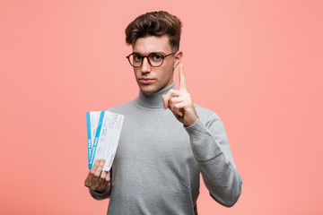 Wall Mural - Young cool man holding an air tickets showing number one with finger.