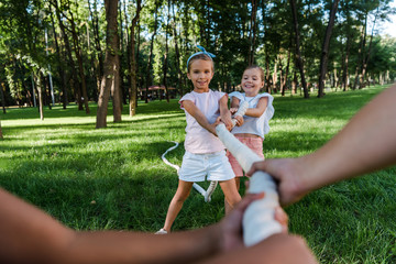 selective focus of cheerful multicultural children competing in tug of war outside
