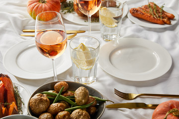 Wall Mural - festive thanksgiving dinner with baked vegetables and glasses with rose wine and lemon water on white tablecloth