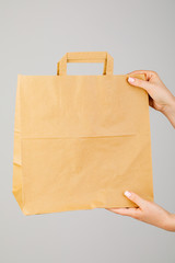 Wall Mural - Close-up of woman holding brown empty paper bag isolated on white background. The concept of service delivery