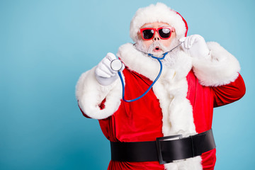 Close-up portrait of his he nice funky bearded Santa wearing mechanical retro phonendoscope making diagnosis listening you isolated over blue turquoise pastel color background