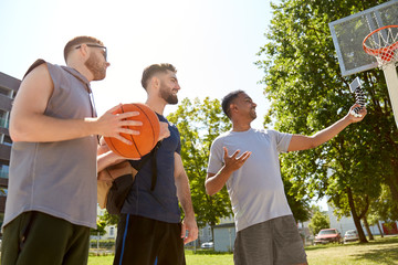 Wall Mural - sport, leisure games and male friendship concept - group of happy men or friends taking selfie by smartphone on tripod on outdoor basketball playground