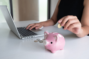 woman hand putting gold coin into pink piggy bank and use laptop for online marketing, step up start up  business to suscess, Saving money for future plan and retirement fund concept