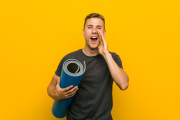 Young caucasian man holding a mat shouting excited to front.