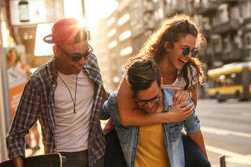 group of friends hangout at the city street. they embrace each other and laughing. one man carrying 