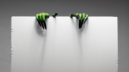 Two green zombie hands are holding blank sheet of paper against grey background.