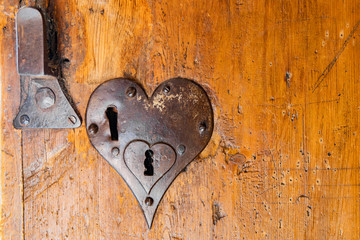 A beautiful heart-shaped door lock on an old weathered wooden door.